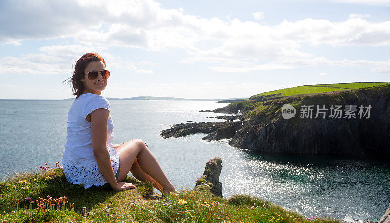 漂亮的女人坐在悬崖上欣赏美丽的风景