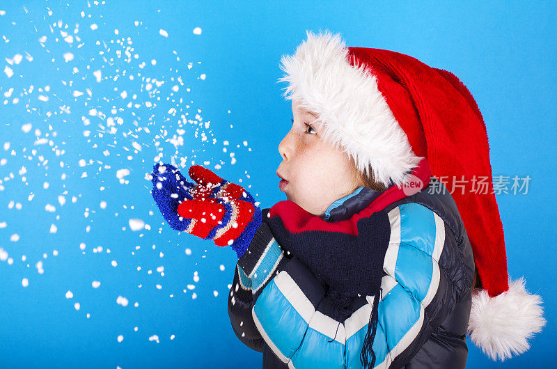 美丽的小女孩戴着圣诞老人的帽子吹着雪花