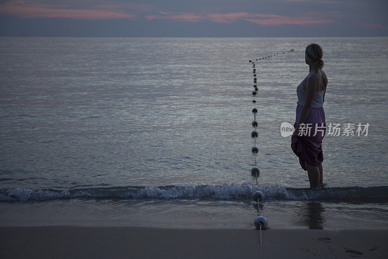 黄昏时分，一名女子在海滩上驻足观赏大海