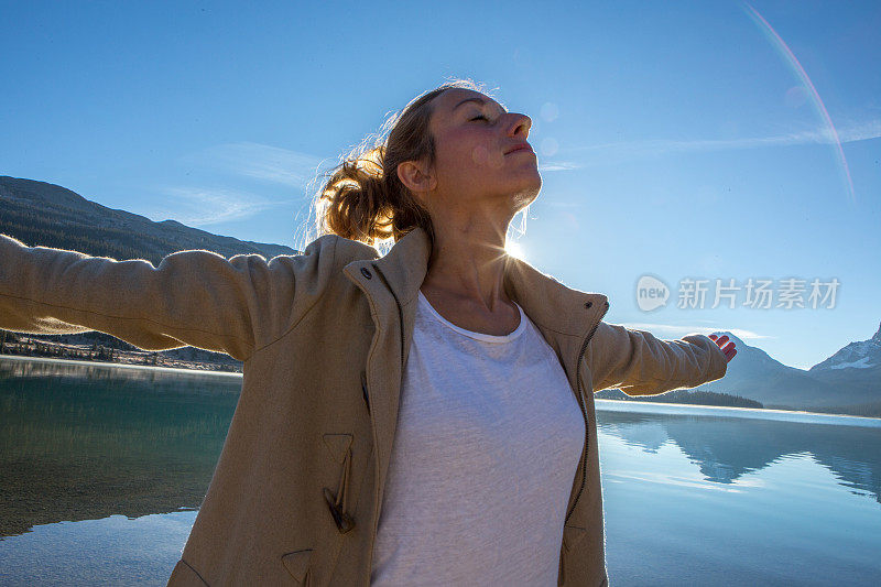 年轻女子在湖边伸开双臂，太阳正在升起