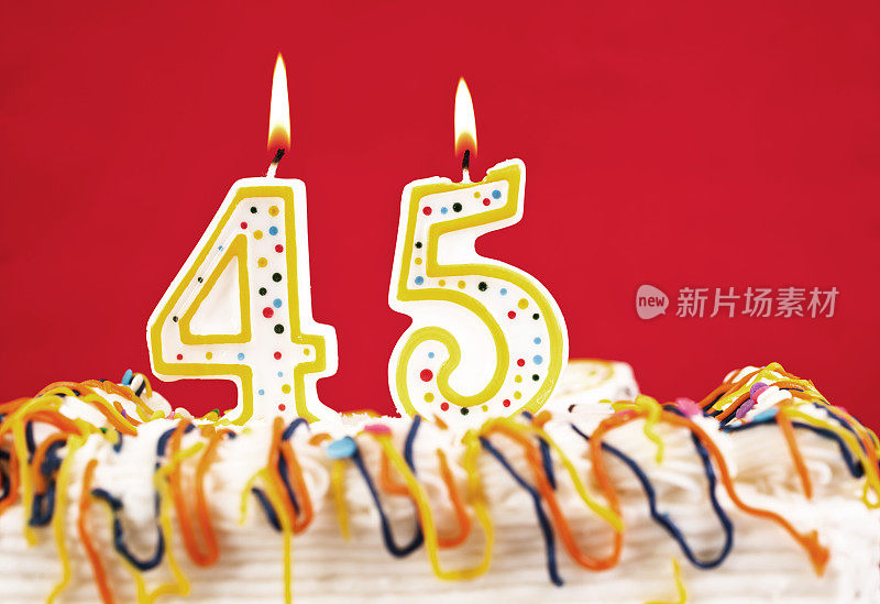用45号燃烧的蜡烛装饰生日蛋糕。红色的背景。