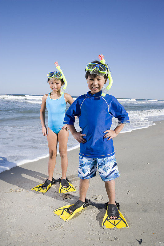 亚洲儿童戴着面罩，呼吸管和脚蹼在海滩上