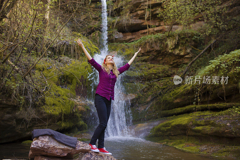 一个女人举着双手站在瀑布边