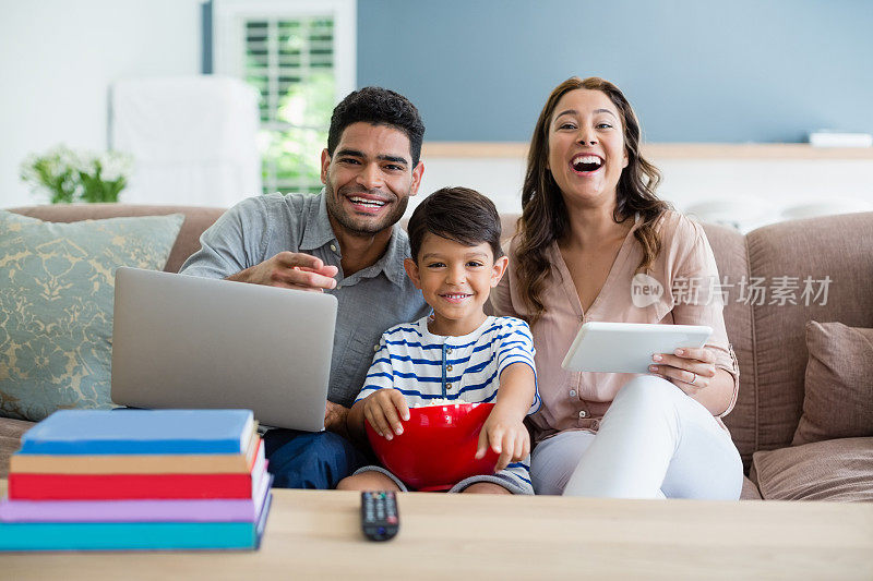 儿子在看电视，而父亲和母亲在家里使用笔记本电脑和数字平板电脑