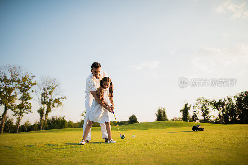 第一次打击。一个男人教他的女儿打高尔夫球，女孩在他的帮助下制作了第一个高尔夫球杆