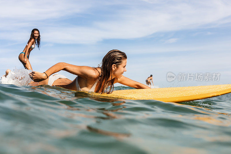 两个漂亮的运动女孩在海里冲浪。