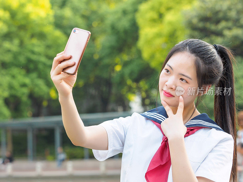 中国女学生穿着校服，用智能手机自拍。