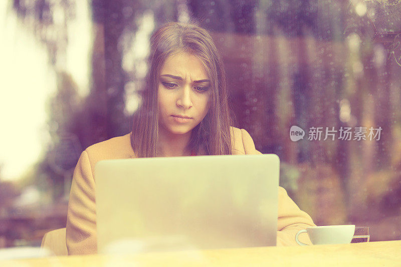 年轻女子坐在咖啡馆的笔记本电脑前，沮丧地看着屏幕，手里拿着屏幕