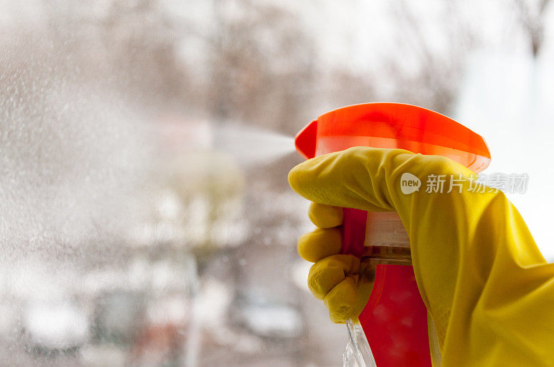 一只手在橡胶手套喷雾意味着清洗玻璃上的窗户。
