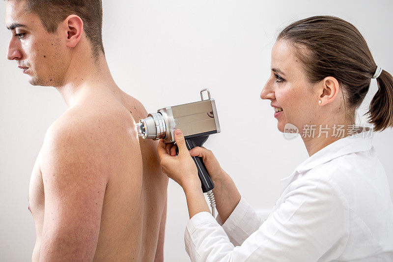 女性皮肤科医生痣映射年轻男子的背部