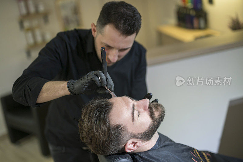 理发师在给一个留胡子的男人刮胡子