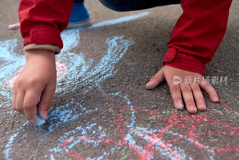 这是一个无法辨认的学龄前男孩的手，用红蓝粉笔在柏油路上画画