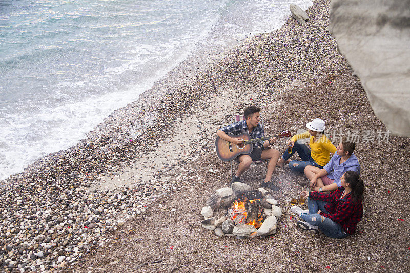 朋友们在沙滩上弹吉他，围着篝火唱歌