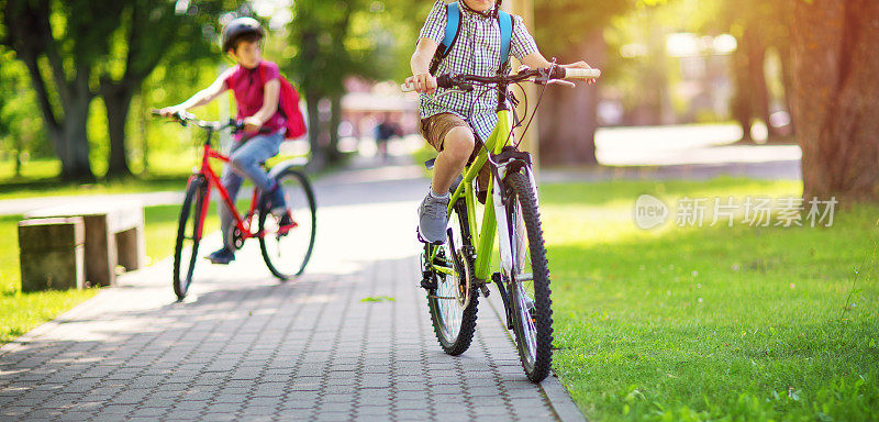 孩子们背着背包在学校附近的公园里骑自行车