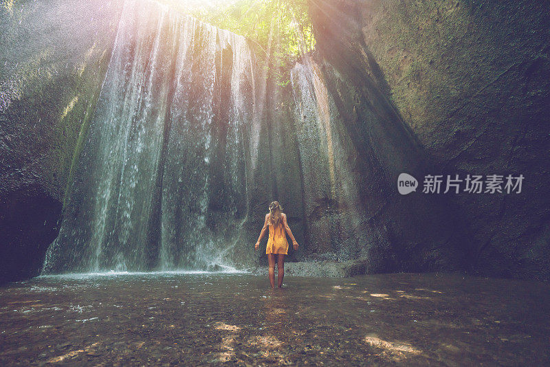 一个女孩站在热带雨林的洞穴里，仰望着从岩石上射下来的壮丽的阳光。人们旅行的奇妙欲望自然的概念