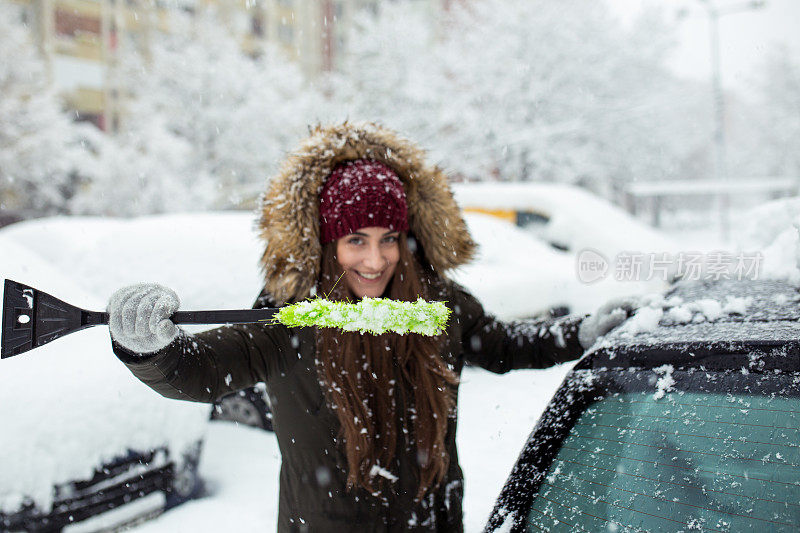 年轻女子在清理车上的积雪