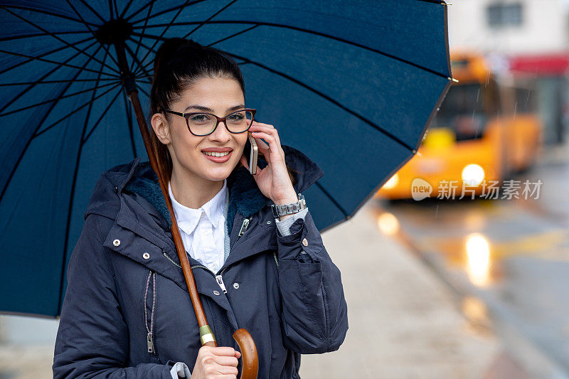 美丽的年轻女子在雨中走在街上，拿着一把伞。