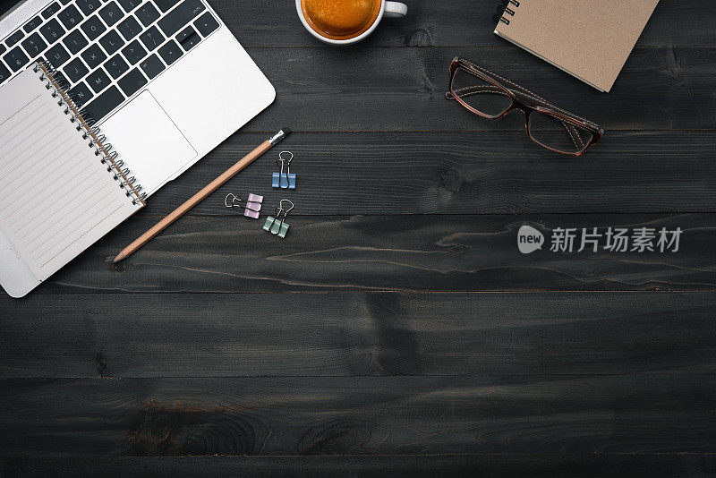 现代深色木质办公桌桌上有笔记本电脑，智能手机和其他用品与一杯咖啡。复制空格，用于在中间输入文本。俯视图，平放。