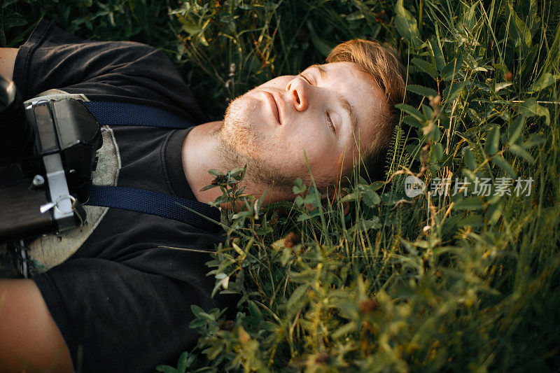 时尚潮男躺在绿色的草地上，在阳光明媚的草地上放松在大气的日落。帅哥在大自然中休息，在山中享受夜晚。空间的文本