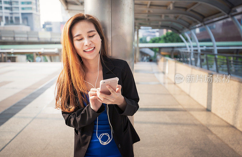 女商人在户外用耳机听音乐，在城市里打电话聊天