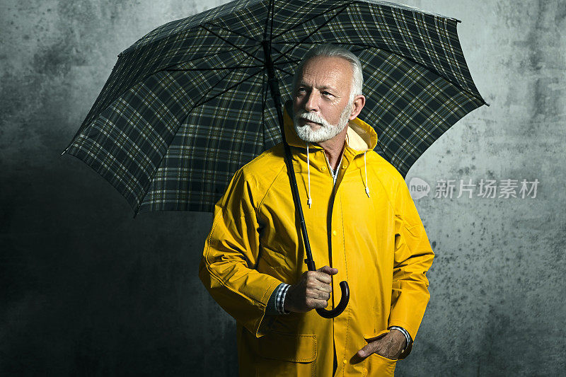 成熟的男人拿着雨衣撑着伞