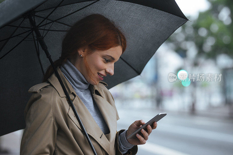 一个拿着雨伞的女人站在街上用手机打字