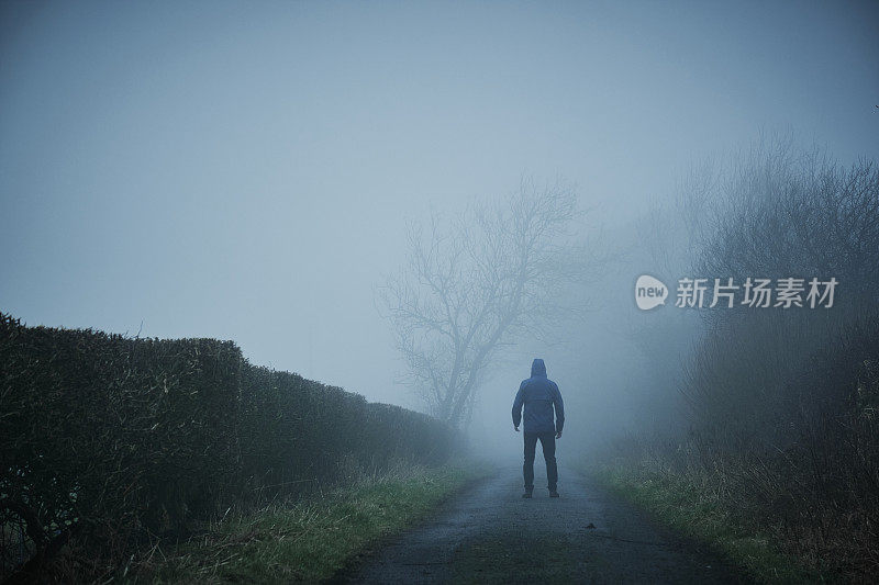 一个人在阴沉的冬日大雾中走在乡间小路上。