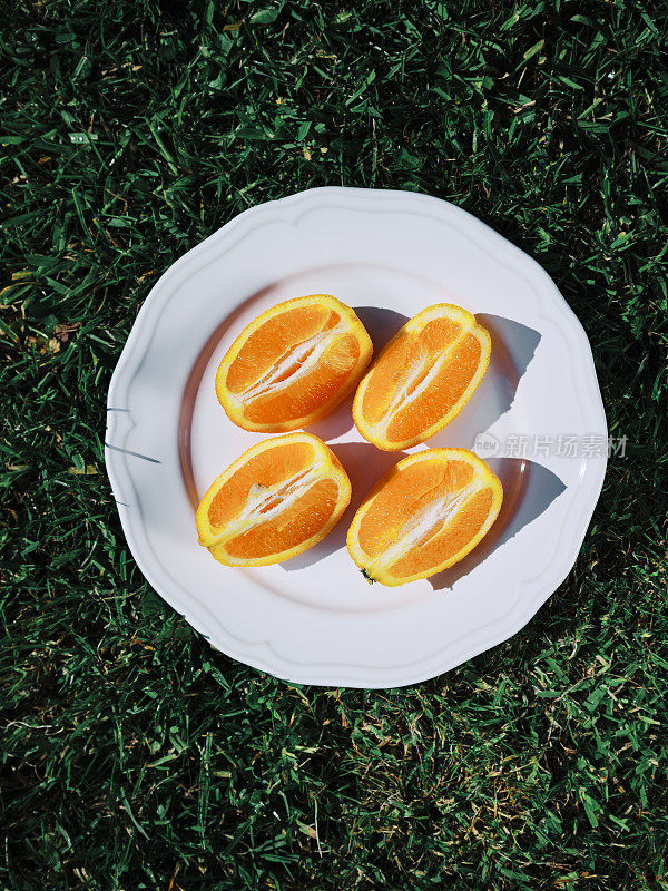 在一个阳光明媚的夏日，外面的绿草地上，在一个白色盘子上切成四分之一的橙子。