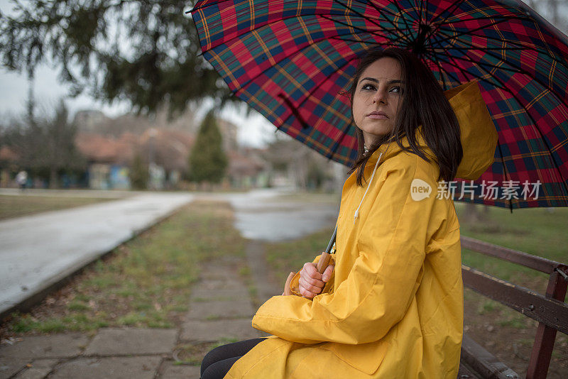 穿着黄色雨衣的年轻女子在公园里度过雨天