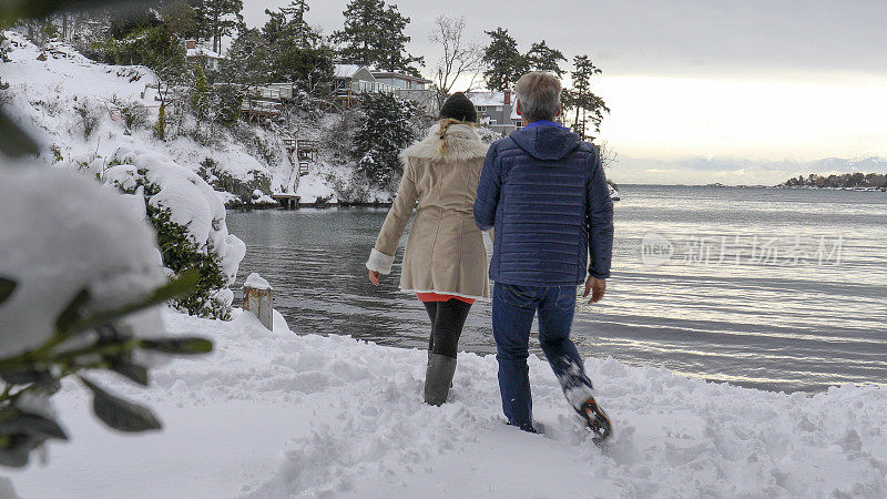 日出时分，一对夫妇走过白雪覆盖的海滩