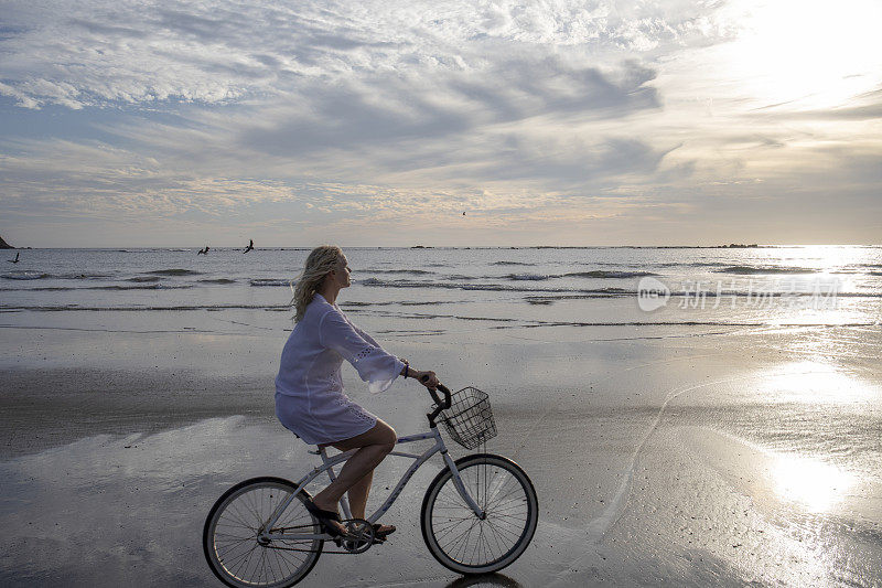 日出时分，一名女子骑着自行车沿着海滩骑行