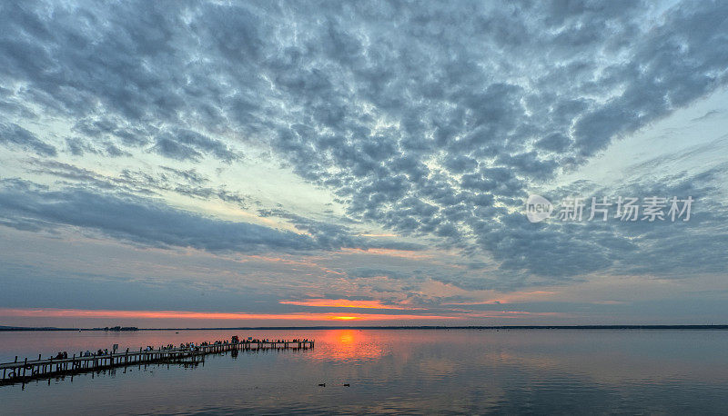 日落时，人们在湖边码头上的剪影与雄伟的云景