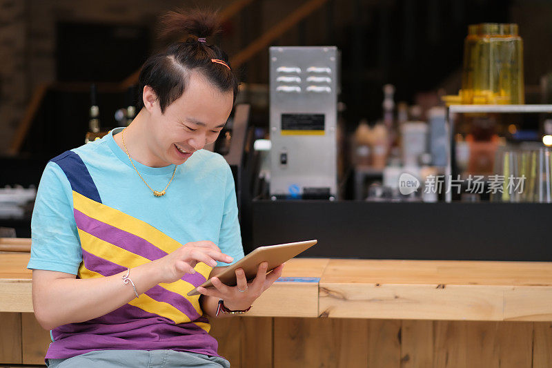 这是一个微笑着的亚洲年轻人在咖啡店里用平板电脑。