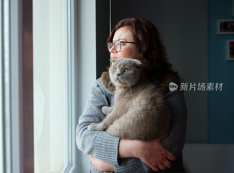 一个年轻女子抱着一只猫向窗外看