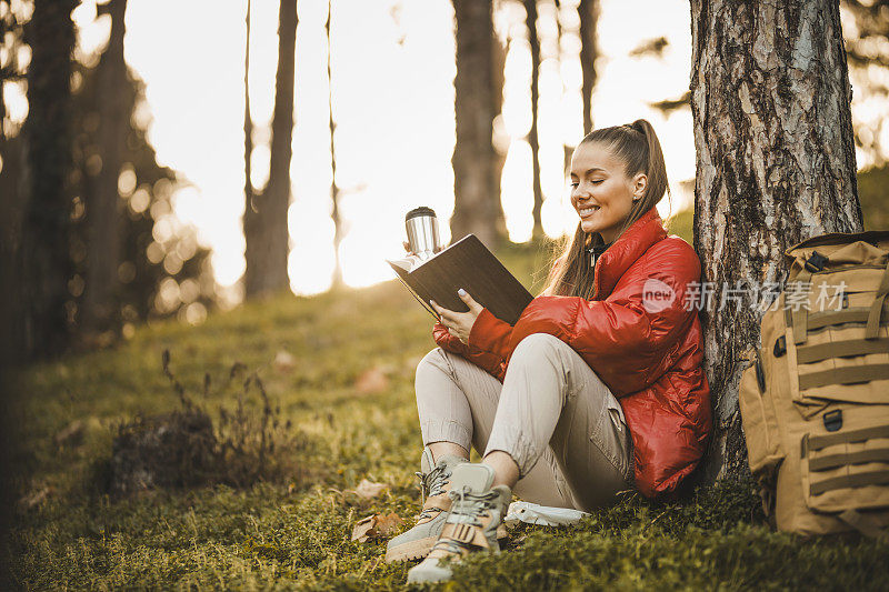 成功的女人徒步登山在日出的山顶-年轻的女人背包上升到山顶。女性徒步旅行者正在休息，阅读一本书和喝咖啡。发现旅游目的地