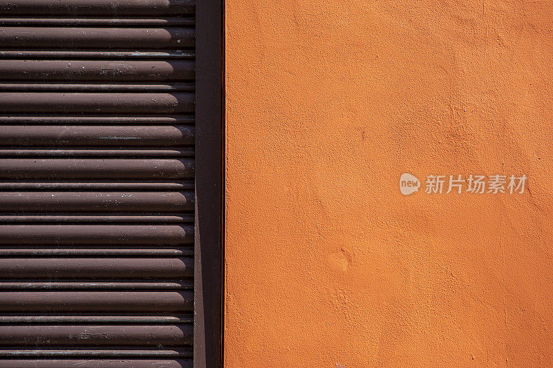 橙色油漆的墙，旁边是紧闭的棕色金属百叶窗