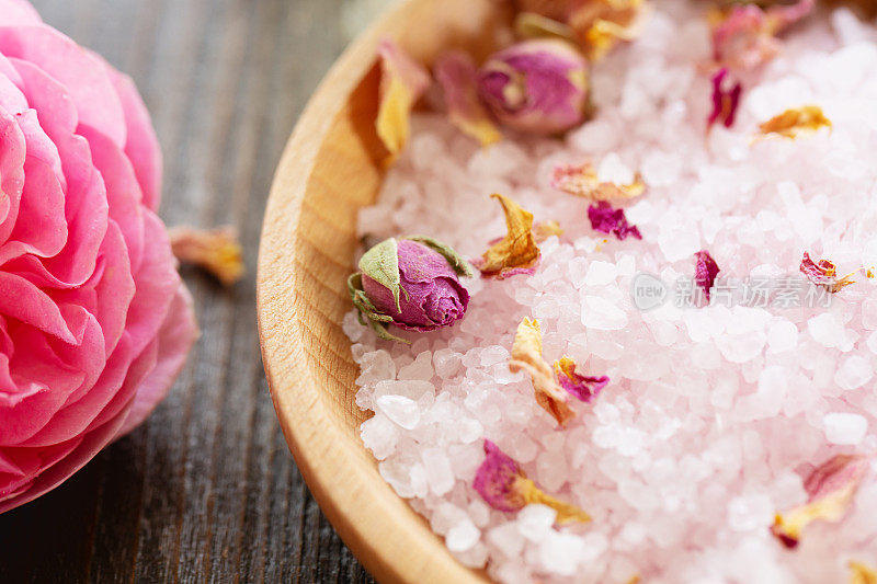 芳香疗法:一个粉红玫瑰的特写镜头和一个木碗与玫瑰香味海盐