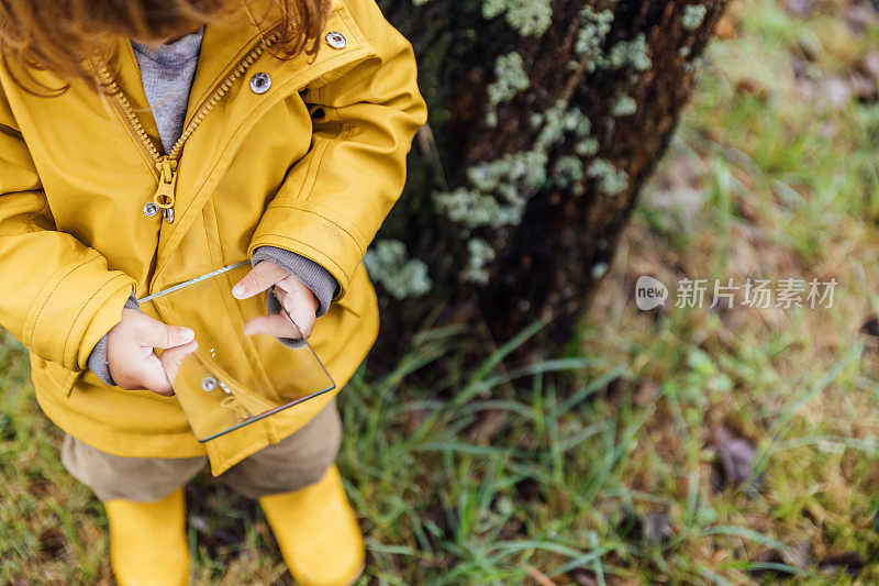 下雨天，一个小女孩拿着一面镜子在公园里玩耍。