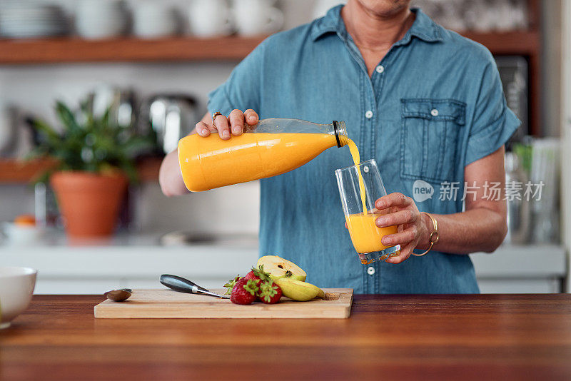 照片中，一个陌生的女人在厨房里准备早餐时倒橙汁