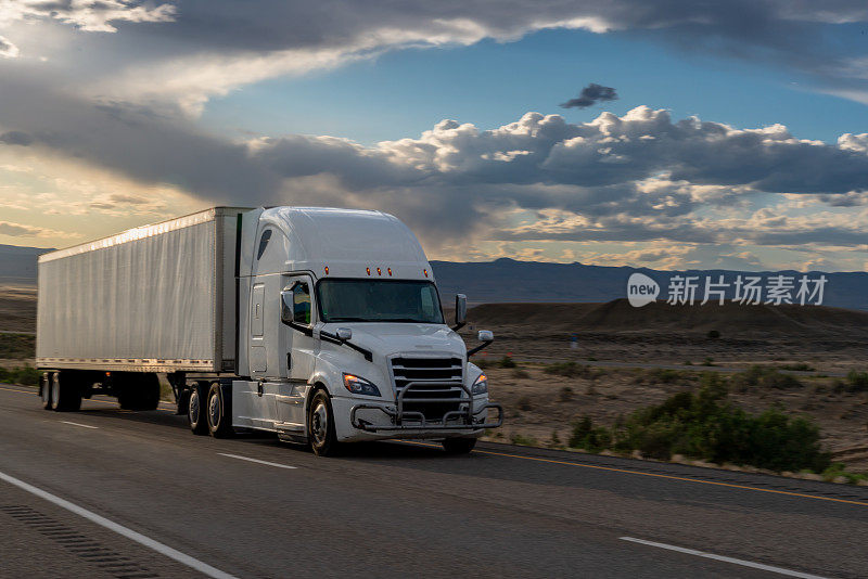 黄昏时分，在戏剧性的天空下，白色半卡车在犹他州沙漠的高速公路上超速行驶