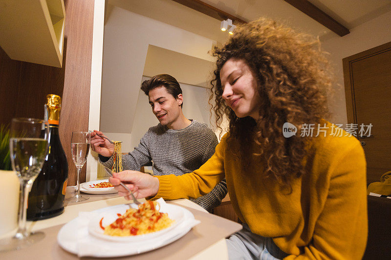 美丽的年轻夫妇在家里喝香槟吃意大利面，享受浪漫的晚餐