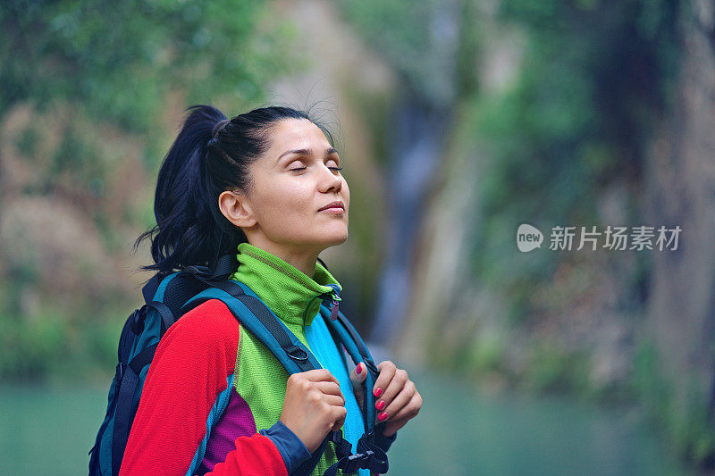 年轻女子在瀑布前呼吸着纯净的空气