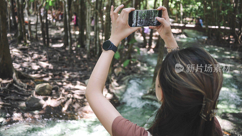 景观翡翠池在热带雨林与亚洲游客妇女用手机拍照视频看惊人的自然蓝色泻湖翡翠池甲米，旅游泰国，旅游目的地亚洲