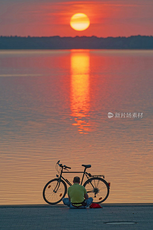 骑自行车的人坐在湖边日落