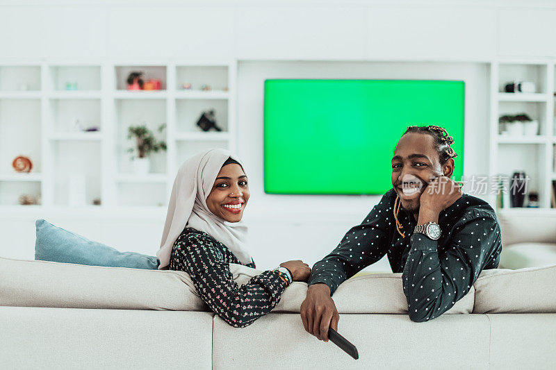 非洲夫妇坐在沙发上一起看电视色度绿幕妇女穿着伊斯兰的希贾布衣服