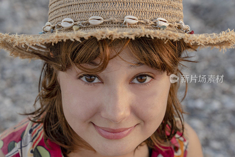 戴着装饰有贝壳的草帽的年轻女子在海滩上玩耍