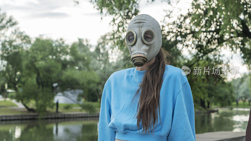 戴着防毒面具的长发女孩站在河岸上。城市中的疏离感。时尚、生态、孤独的概念。