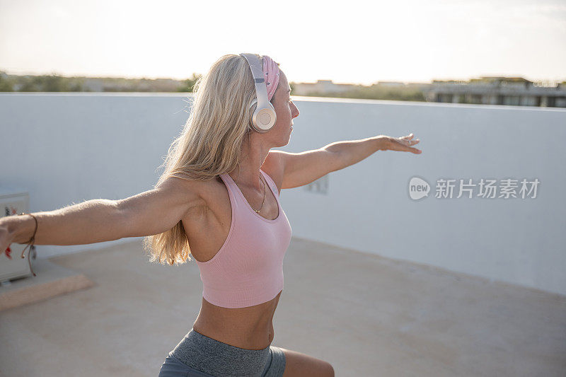 年轻女子喜欢在日出时在屋顶上练习瑜伽，武士姿势