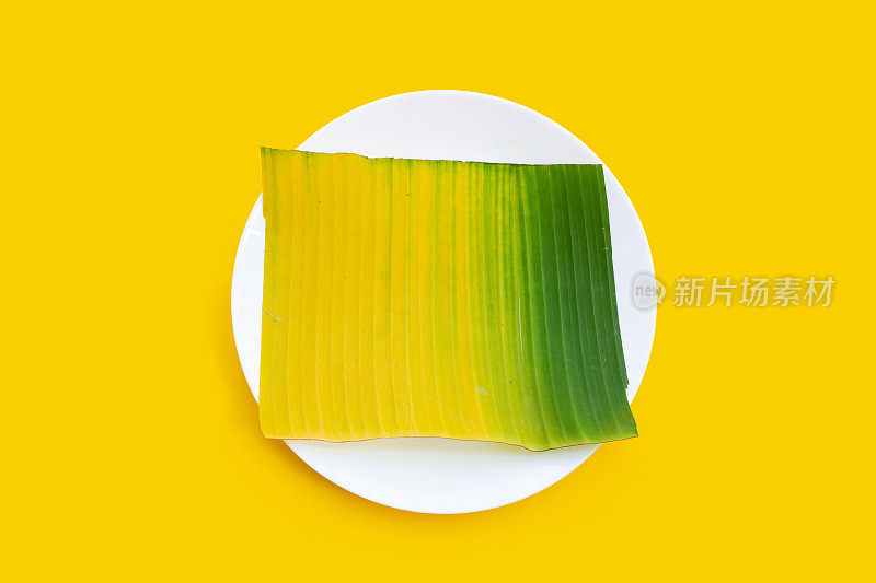 黄绿色的芭蕉叶在白色的盘子在黄色的背景。