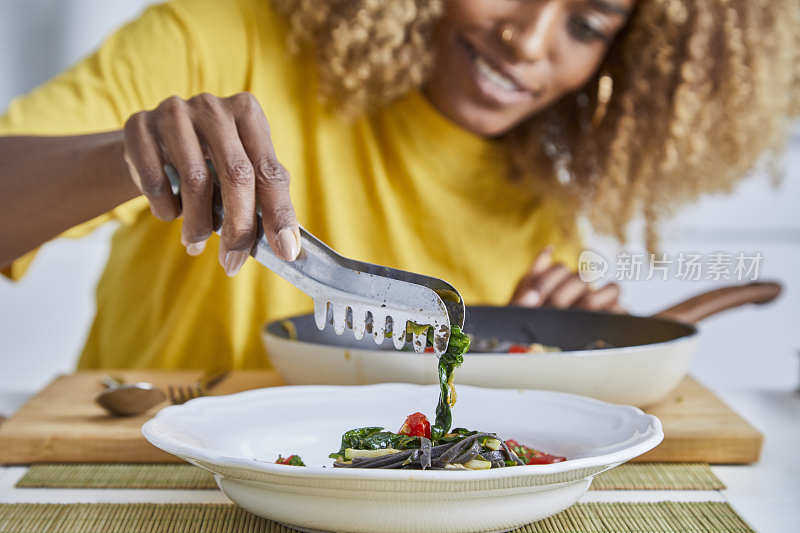 一个女人在厨房准备食物，往盘子里放意大利面